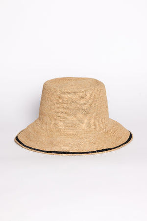 The STRIPE EDGE MODERN CROCHET BUCKET HAT by Velvet by Graham & Spencer is a woven beige bucket hat with a wide brim and a thin black stripe near the edge, shown on a plain white background.