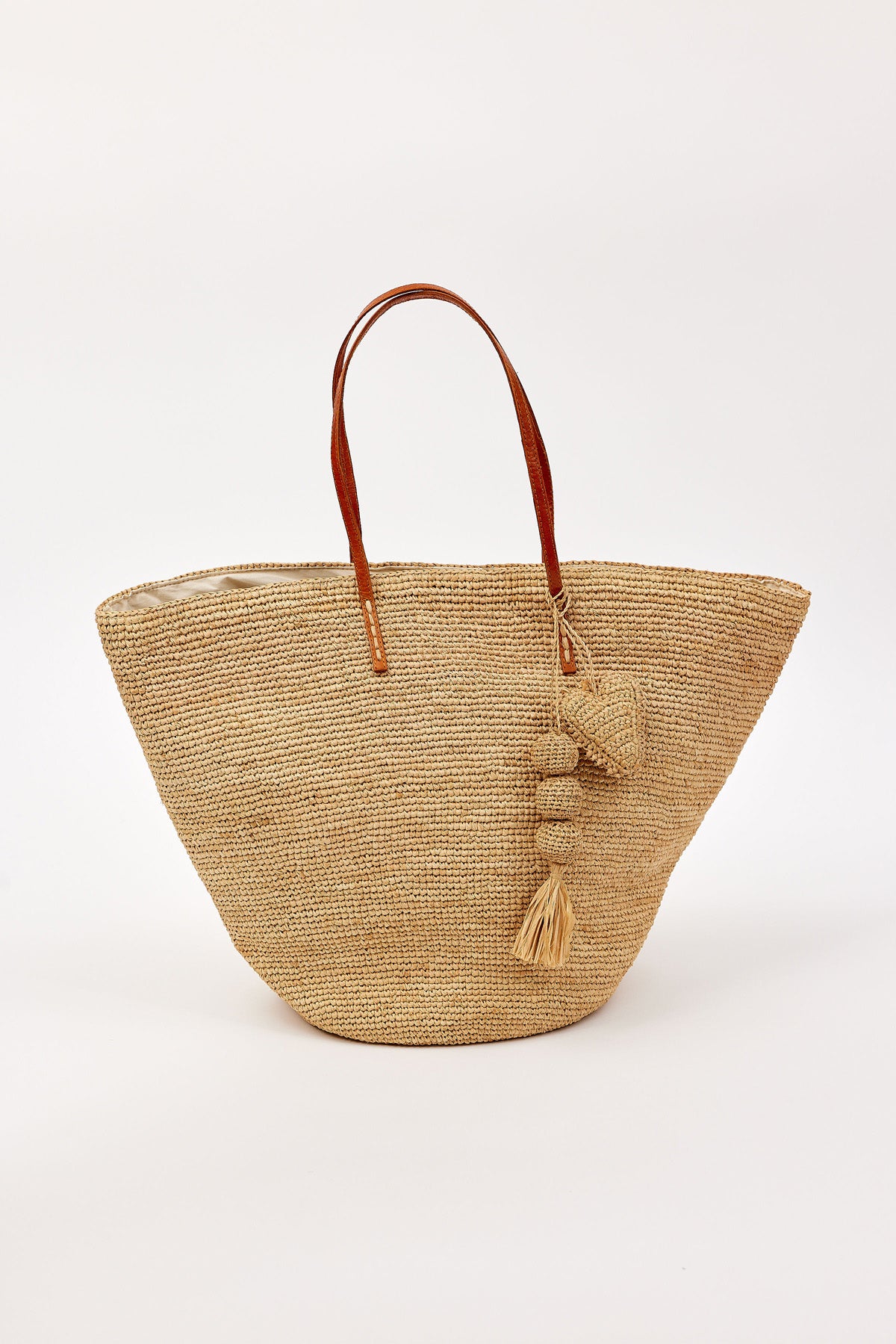 The MARY TOTE by Velvet by Graham & Spencer features woven straw construction, brown leather handles, and decorative tassels, displayed against a plain white background.-41323182293185