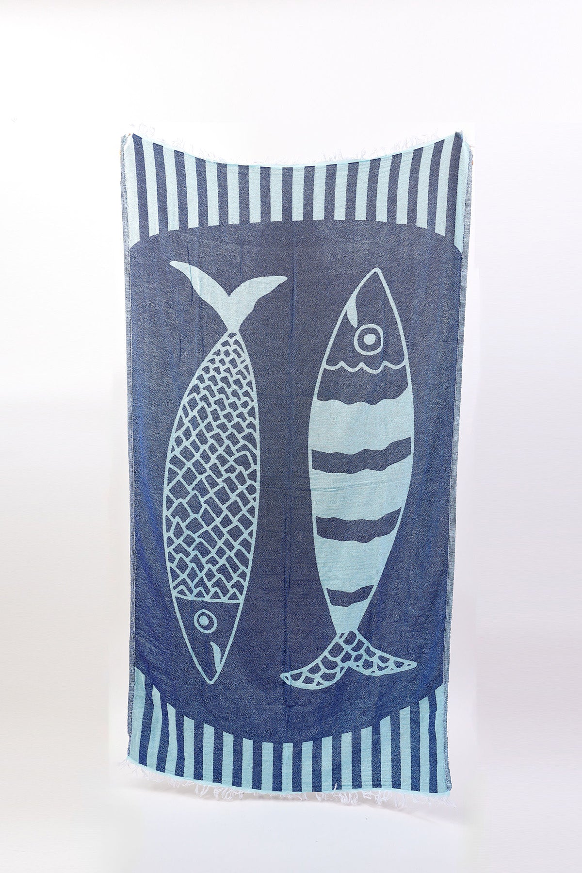 The NOVELTY TURKISH TOWEL by Velvet by Graham & Spencer is a rectangular blue towel with two large fish illustrations in unique patterns, inspired by Turkish loomed designs and bordered by vertical stripes.