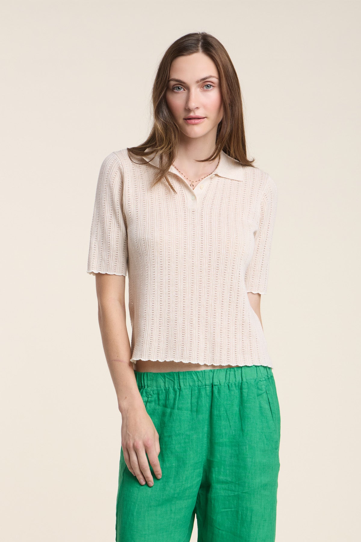 A woman wears the DANAE SWEATER POLO by Velvet by Graham & Spencer in light beige, paired with green linen pants, standing against a plain light background.-41526974054593