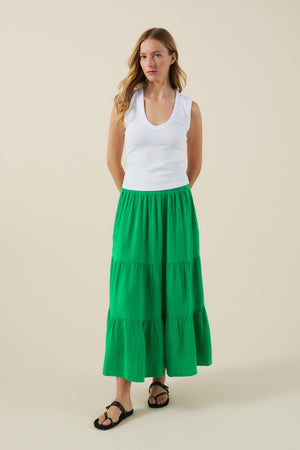 A woman stands against a plain background wearing a white sleeveless top, black sandals, and the DANIELLE SKIRT by Velvet by Graham & Spencer—a green cotton gauze skirt with an elastic waist that falls midi to maxi length.