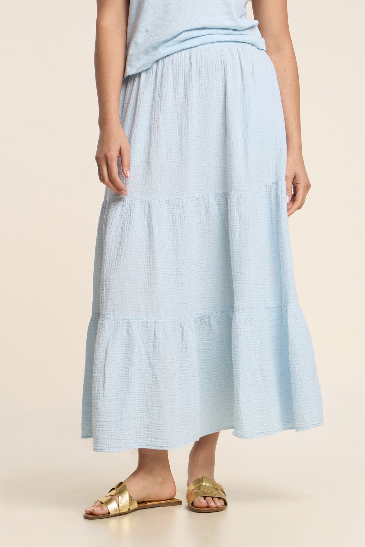 A person wearing the DANIELLE SKIRT by Velvet by Graham & Spencer in light blue cotton gauze, paired with a matching top and gold sandals, stands against a neutral background.-41338478854337