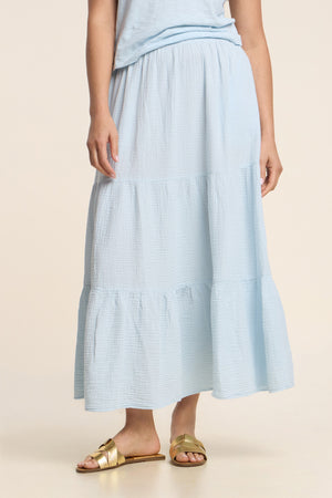A person wearing the DANIELLE SKIRT by Velvet by Graham & Spencer in light blue cotton gauze, paired with a matching top and gold sandals, stands against a neutral background.