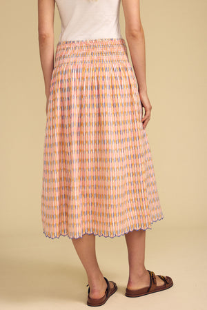 A person in a white top and brown sandals models the DEBORAH SKIRT by Velvet by Graham & Spencer—a printed cotton skirt with a smocked elastic waist—seen from the back against a beige background.