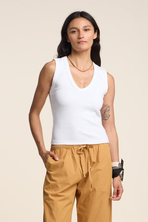 A person with long dark hair wears the DEMI TANK TOP by Velvet by Graham & Spencer, paired with tan drawstring pants, standing against a neutral background.