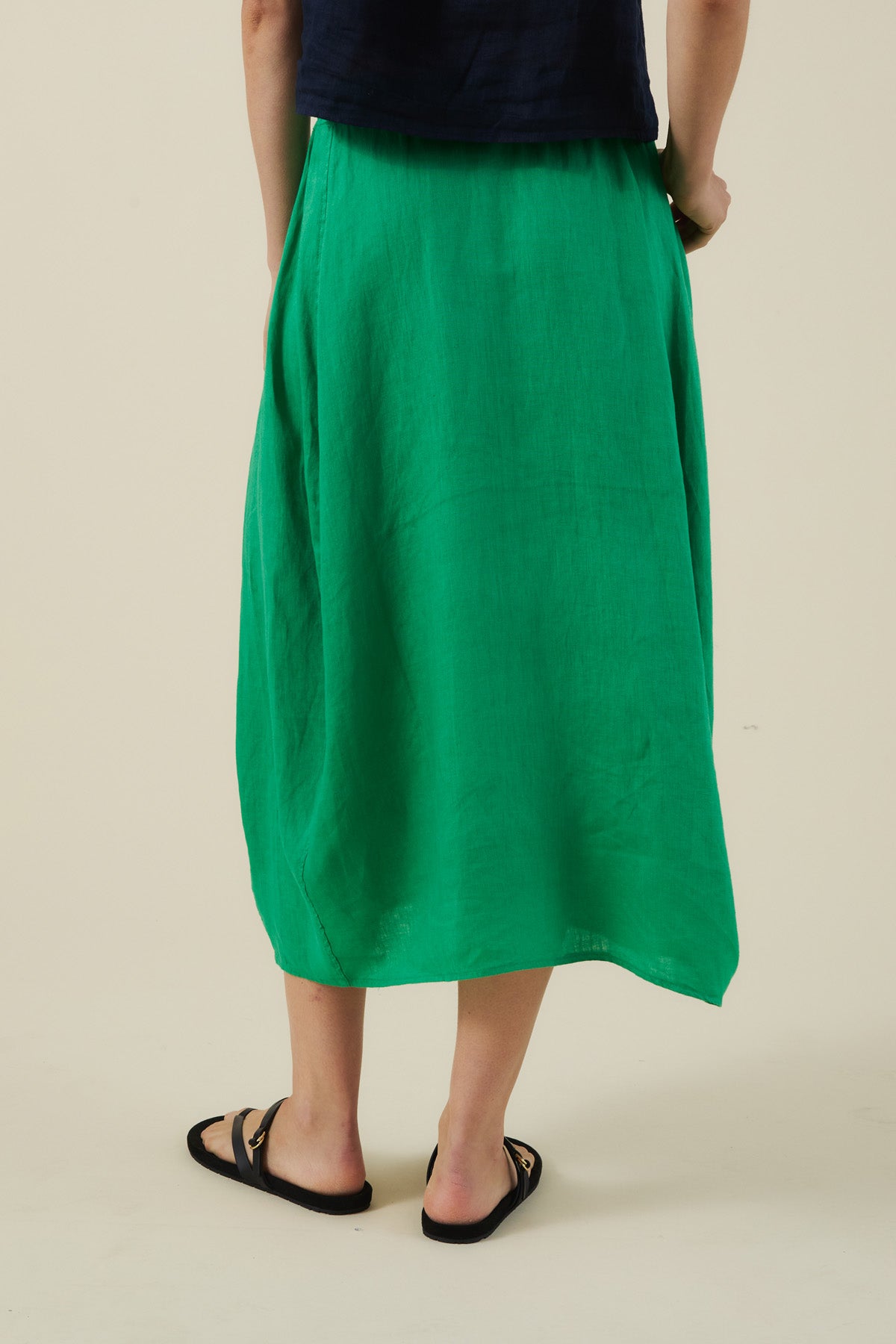 A person wears a black top, black sandals, and the FAE LINEN SKIRT by Velvet by Graham & Spencer—a bright green A-line linen skirt—standing with their back to the camera against a plain light background.-41527342497985
