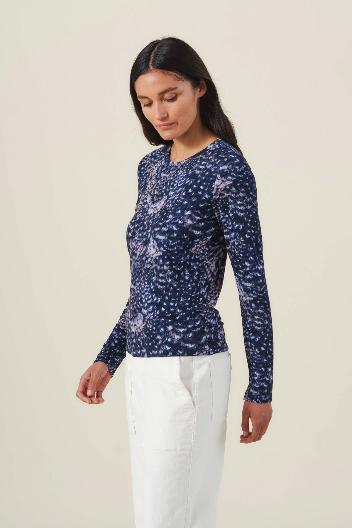 A woman wearing a dark blue, long-sleeved LILIAN PRINTED TEE and white trousers.
