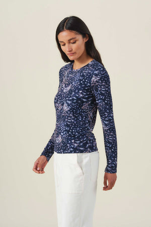 A woman wearing a dark blue, long-sleeved LILIAN PRINTED TEE and white trousers.