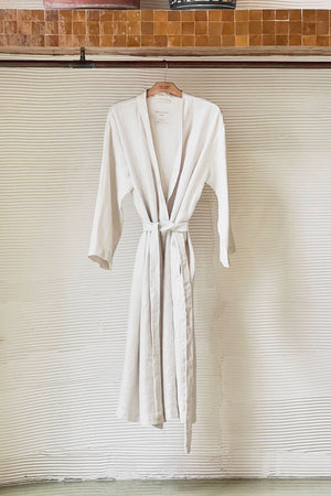 Jenny Graham Linen Robe in beach on hanger near textured wall