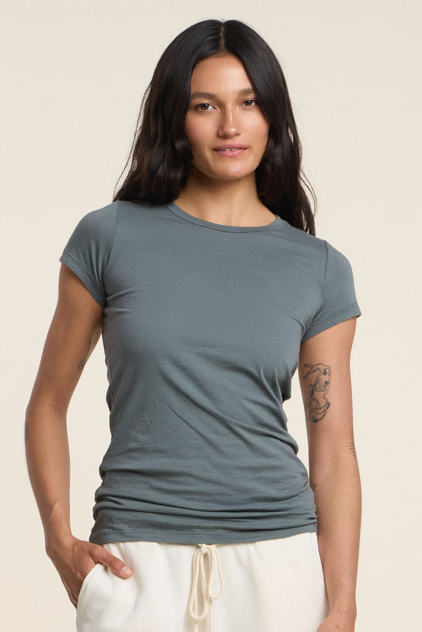 A woman with long dark hair wears the JEMMA TEE by Velvet by Graham & Spencer in gray and light drawstring pants, standing against a plain background.