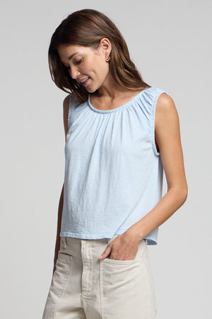 A woman wears the JUNA TANK TOP by Velvet by Graham & Spencer with light pants, one hand in her pocket as she looks down and smiles.