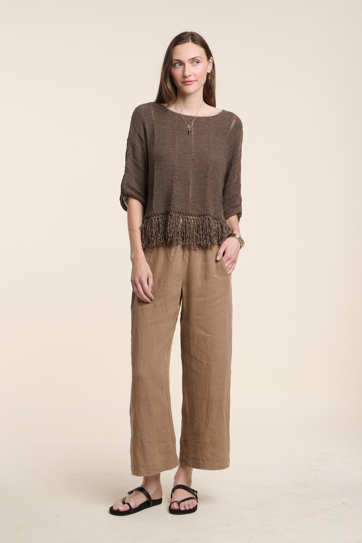 A woman poses against a plain background in the Velvet by Graham & Spencer KATARINA SWEATER, styled with loose tan pants, black sandals, and simple jewelry.