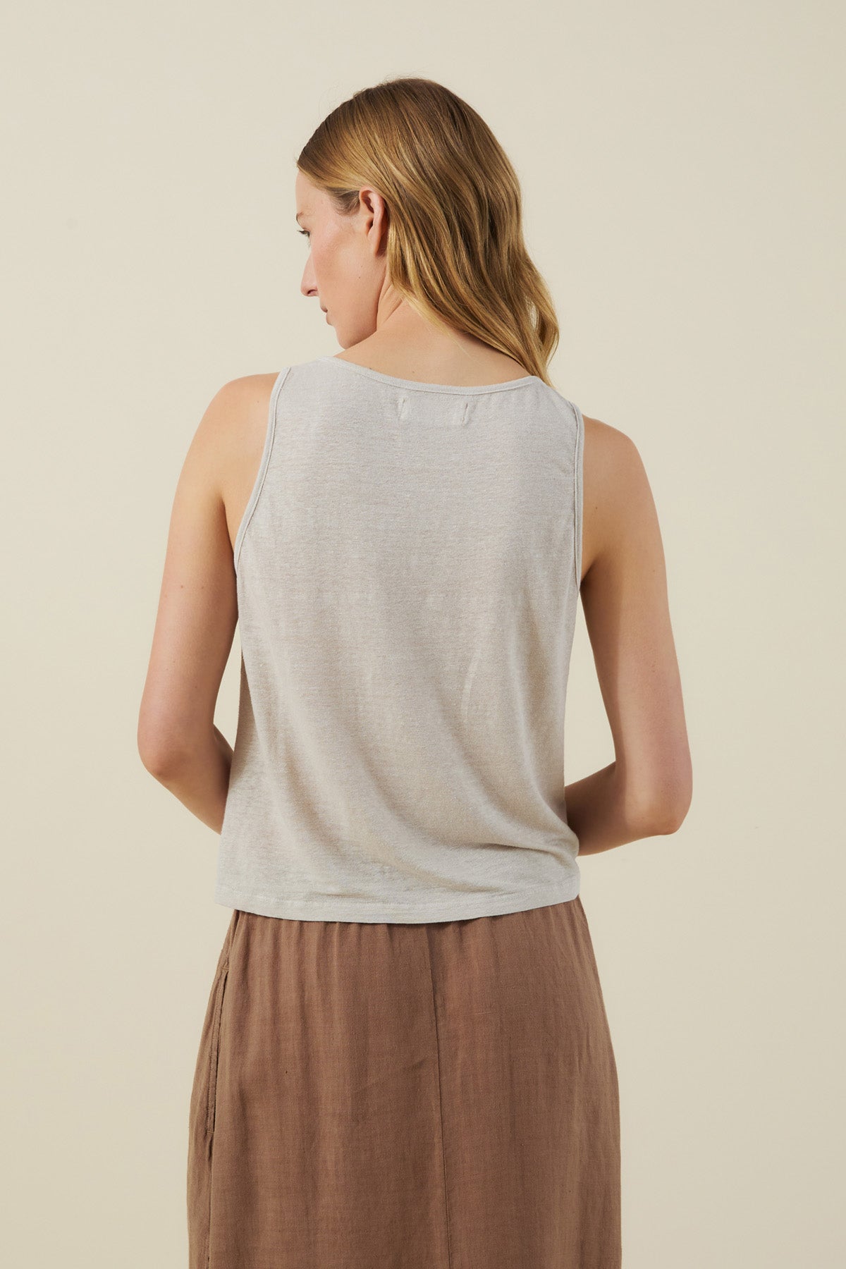 A woman with light brown hair faces away, wearing the KYLIE TANK TOP by Velvet by Graham & Spencer and a brown skirt, set against a plain light background.-41601681457345