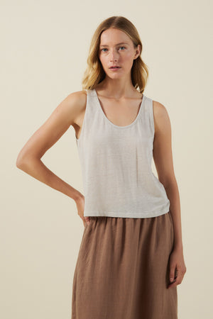 A woman poses against a plain background wearing the KYLIE TANK TOP by Velvet by Graham & Spencer in light gray with a scoop neckline and a brown skirt, her hand resting on her hip.