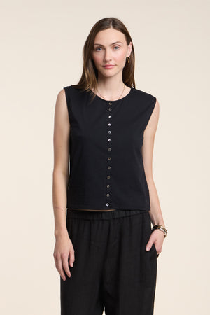 A woman wears the LACY TOP by Velvet by Graham & Spencer—a sleeveless black button-up—paired with black pants, standing against a plain light background.