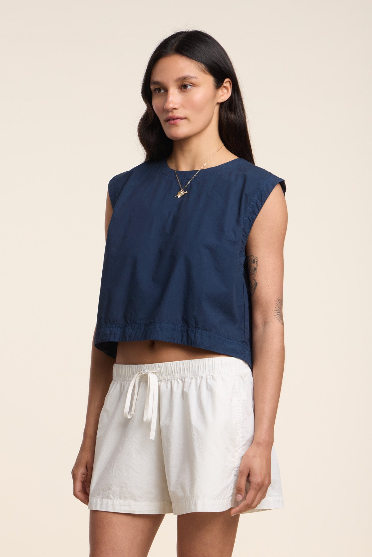 A person wears the LARISSA TOP by Velvet by Graham & Spencer—a navy cotton poplin sleeveless cropped top—paired with white drawstring shorts, standing against a neutral background.