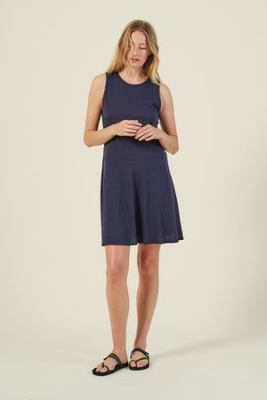 A woman stands against a plain background, wearing the sleeveless LOEN DRESS in navy by Velvet by Graham & Spencer and black sandals.