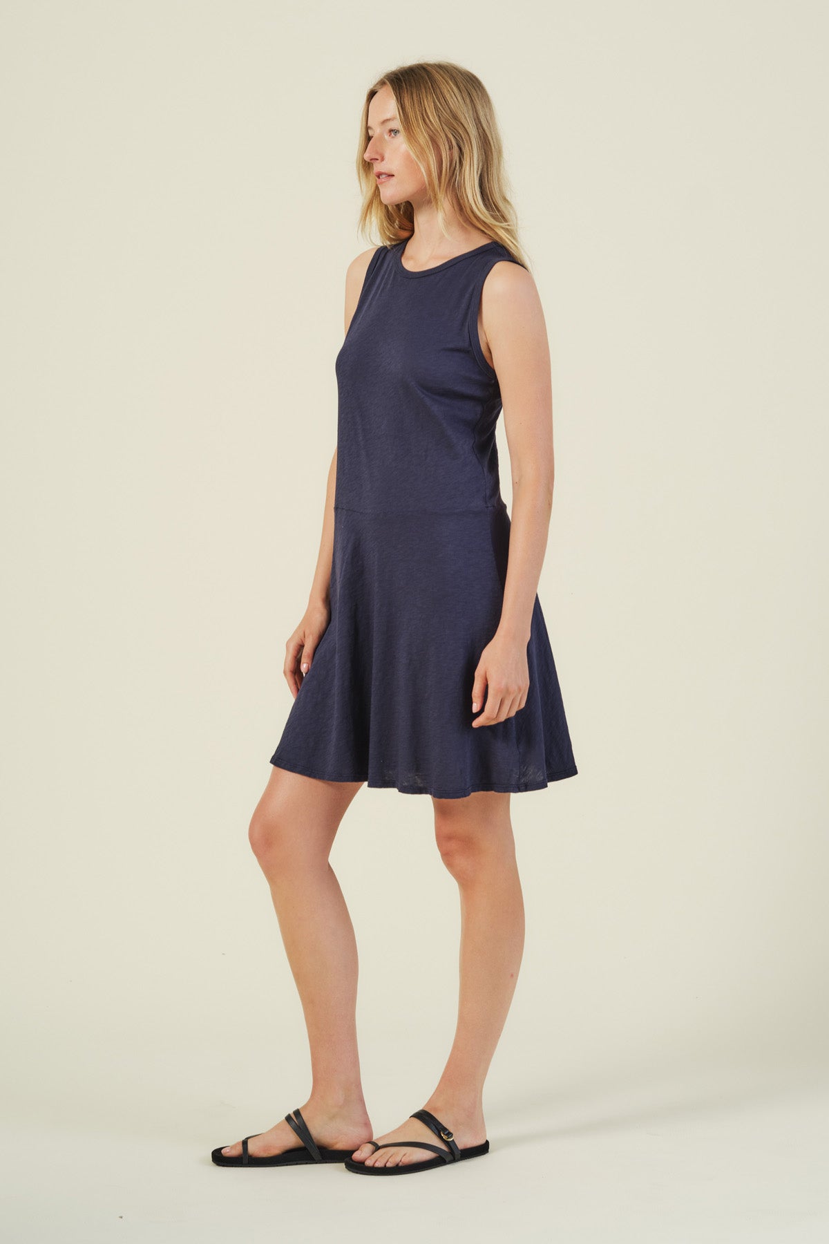 A woman stands against a plain background wearing the LOEN DRESS, a sleeveless navy blue cotton tank dress by Velvet by Graham & Spencer, paired with black sandals.
