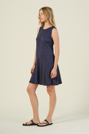 A woman stands against a plain background wearing the LOEN DRESS, a sleeveless navy blue cotton tank dress by Velvet by Graham & Spencer, paired with black sandals.