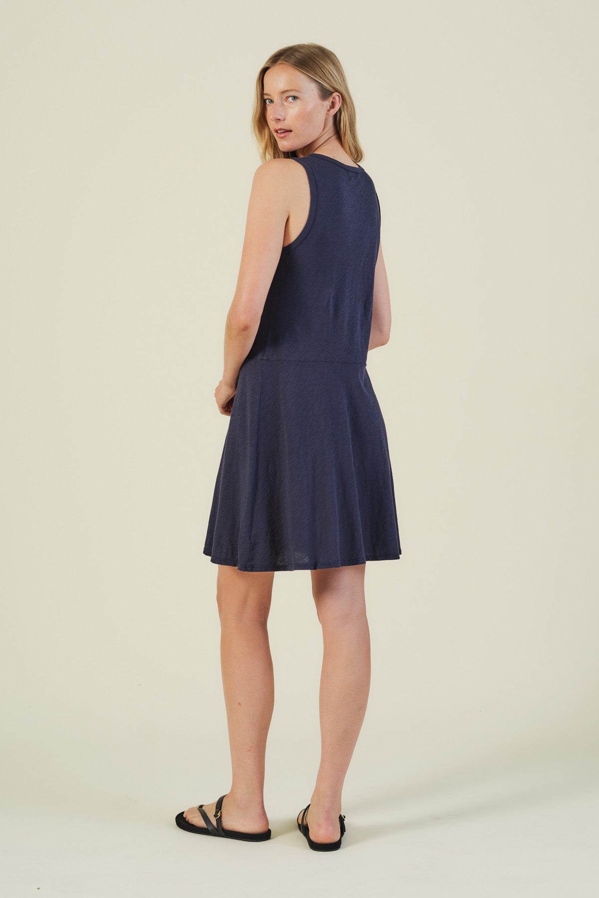 A woman faces slightly away from the camera wearing the LOEN DRESS by Velvet by Graham & Spencer—a sleeveless cotton tank dress—paired with black sandals, set against a simple light background.-41527065280705