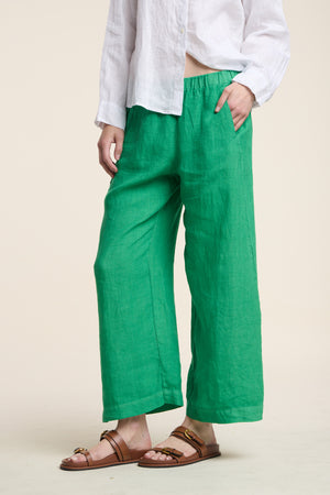 Wearing the LOLA LINEN PANT by Velvet by Graham & Spencer in bright green, paired with a white long-sleeve shirt and brown sandals, standing against a plain light background.
