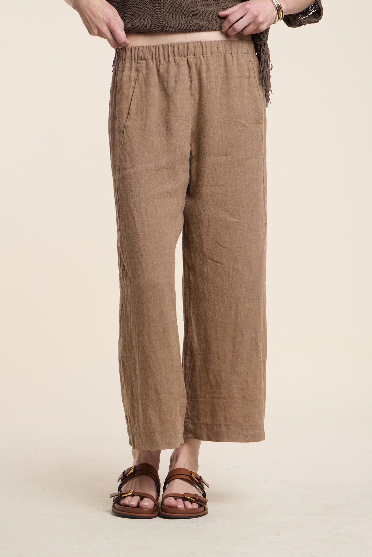 Model wears the LOLA LINEN PANT by Velvet by Graham & Spencer—lightweight, cropped, light brown wide leg linen pants with an elastic waistband—styled with brown sandals and top against a neutral background.