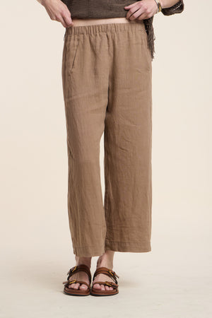 Model wears the LOLA LINEN PANT by Velvet by Graham & Spencer—lightweight, cropped, light brown wide leg linen pants with an elastic waistband—styled with brown sandals and top against a neutral background.