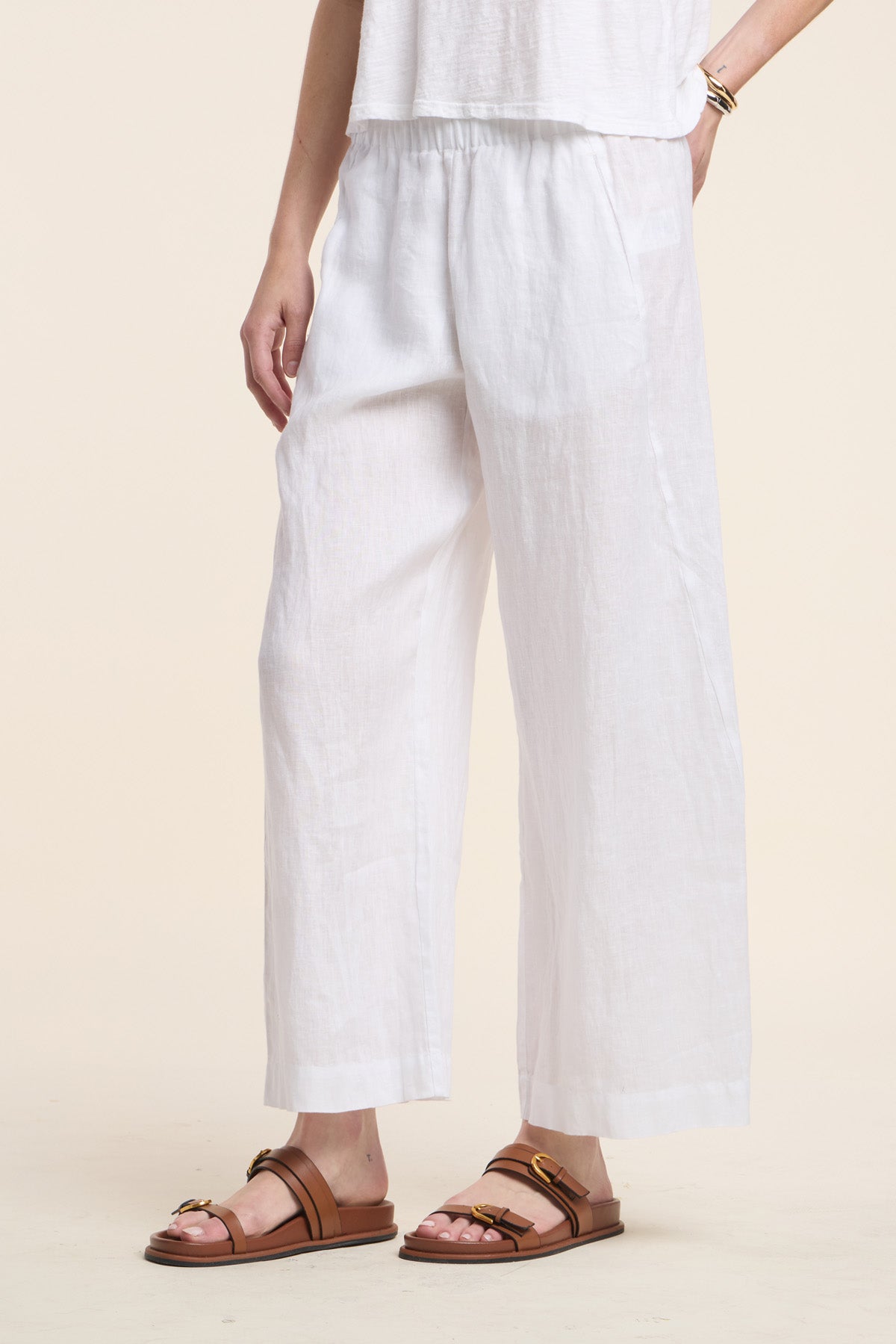 A person wearing the LOLA LINEN PANT by Velvet by Graham & Spencer in white, paired with a white top and brown sandals, stands against a neutral background. Only the lower torso and legs are visible.-41803019780289