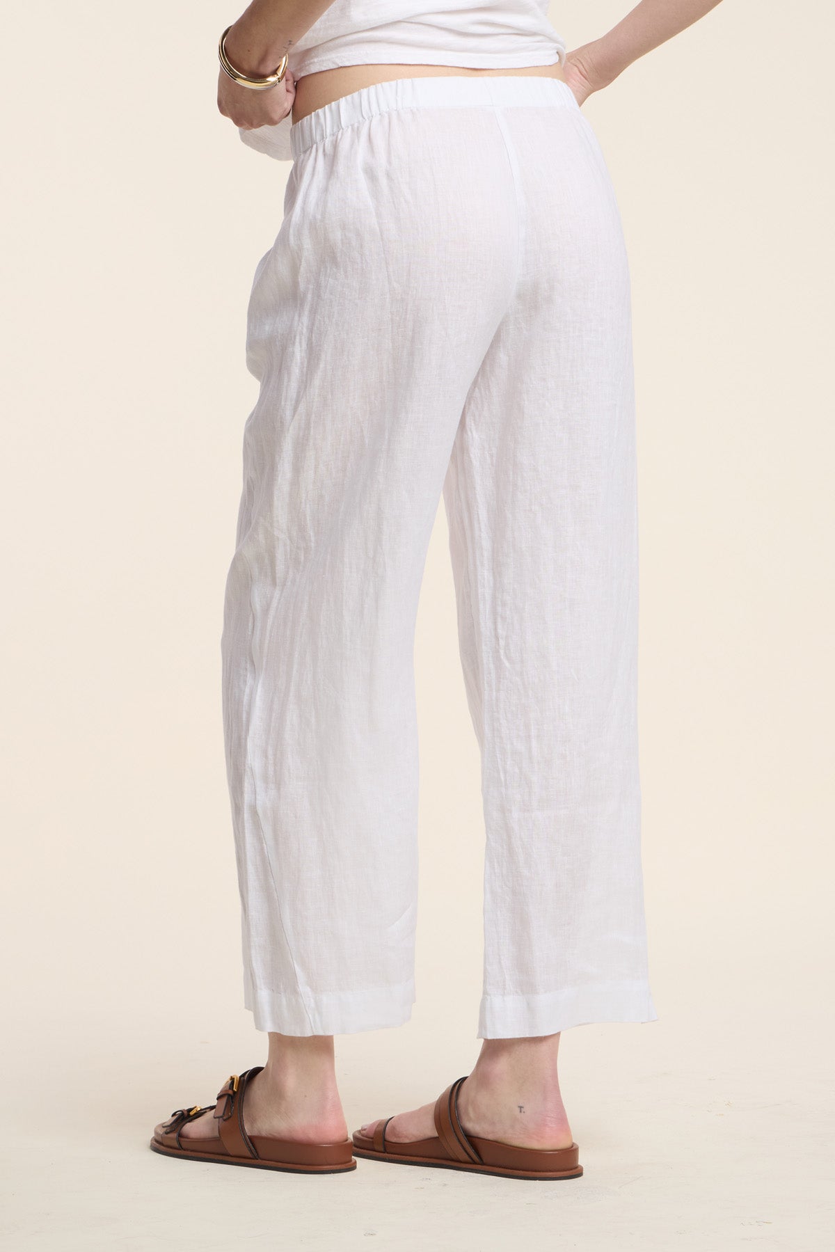 A person wearing the Velvet by Graham & Spencer LOLA LINEN PANT and brown sandals stands against a plain light background, shown from the back waist down.-41803019747521
