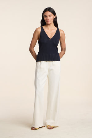 A person stands against a plain background wearing the LORENA TANK TOP by Velvet by Graham & Spencer, paired with white wide-leg pants and yellow sandals—a breezy look perfect for layering in warm weather.