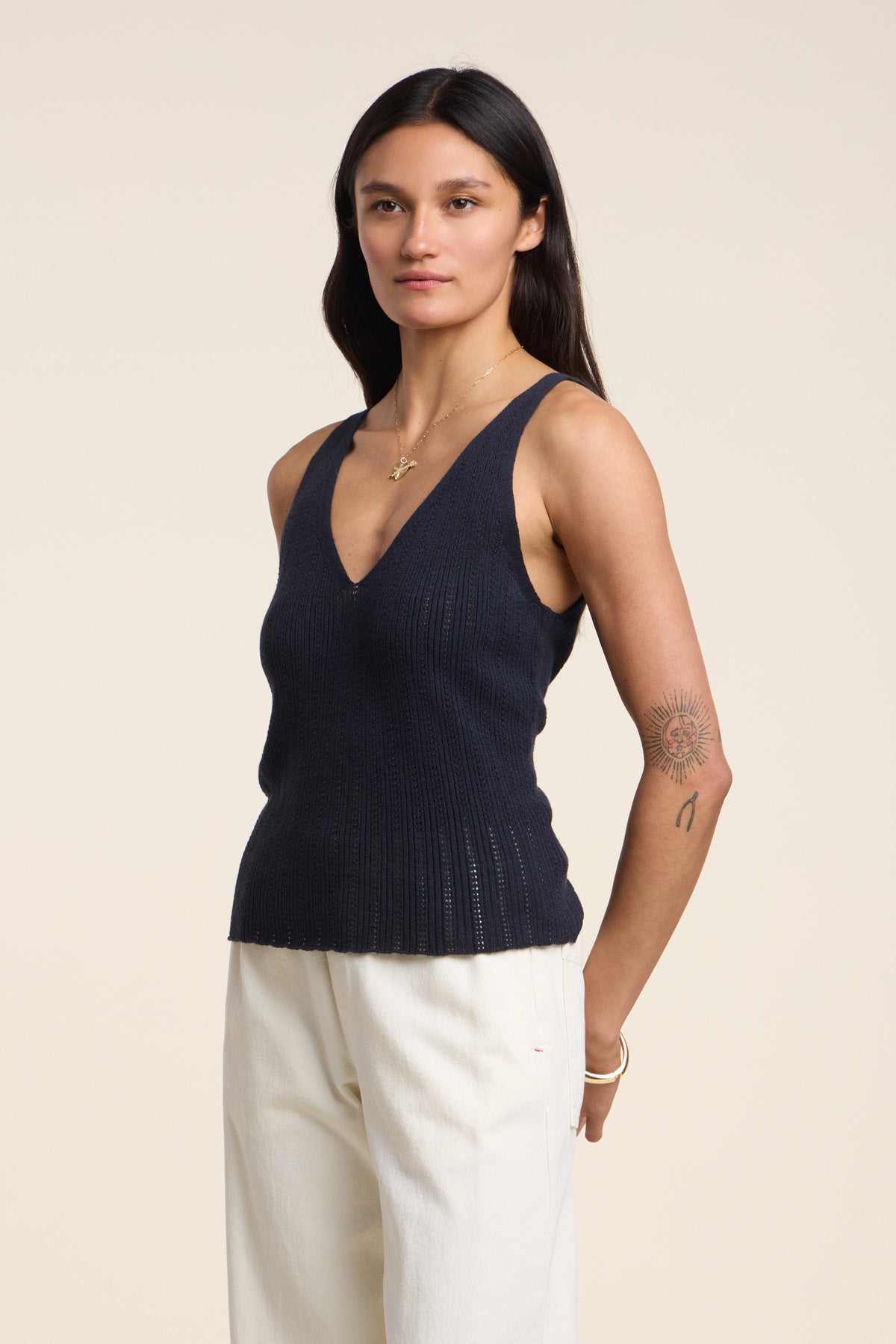 A person with long dark hair models the LORENA TANK TOP by Velvet by Graham & Spencer—an organic cotton-linen navy pointelle sweater tank—paired with white pants, ideal for warm-weather layering against a plain background.-41527093199041