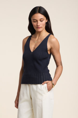 A woman models the LORENA TANK TOP by Velvet by Graham & Spencer—a navy pointelle sweater tank in organic cotton-linen—paired with white pants against a neutral backdrop, ideal for stylish warm-weather layering.