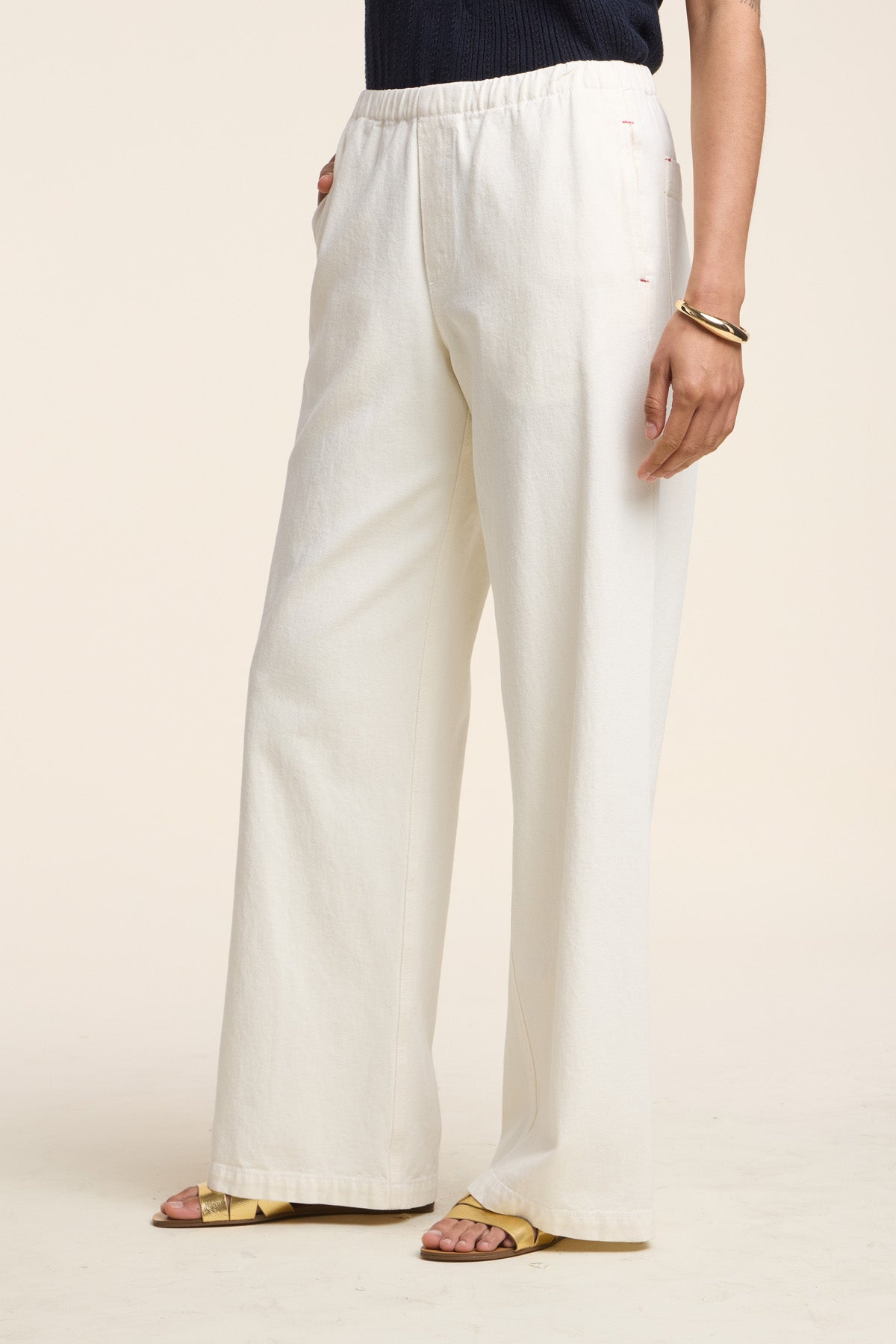 Wearing the LOUISE DENIM PANT by Velvet by Graham & Spencer—loose-fitting, high-waisted off-white denim with a relaxed silhouette—paired with a dark top, yellow sandals, and gold bangles against a plain background.-Hover Image