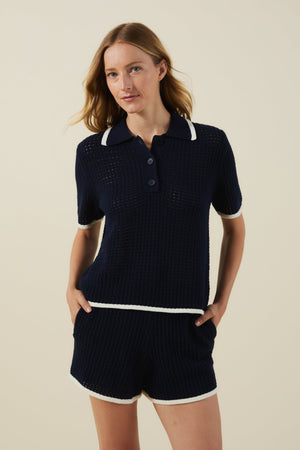A woman in the LUMAE SWEATER POLO by Velvet by Graham & Spencer stands against a plain background—a sporty-chic, navy mesh top perfect for your warm-weather wardrobe.