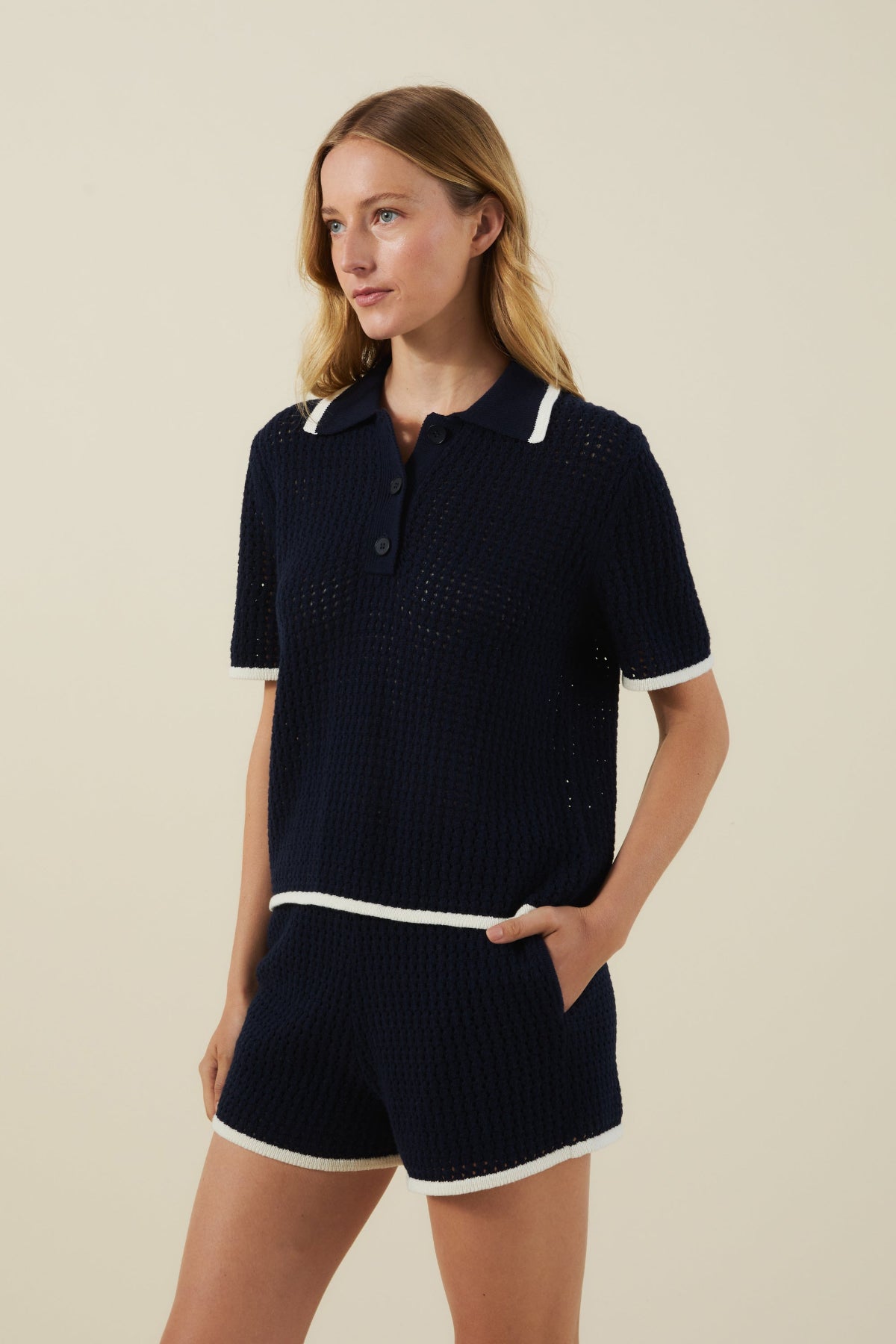 A woman wears the LUMAE SWEATER POLO by Velvet by Graham & Spencer— a sporty-chic navy cotton mesh top with white trim, ideal for warm-weather looks, shown against a plain beige background.-41460579139777