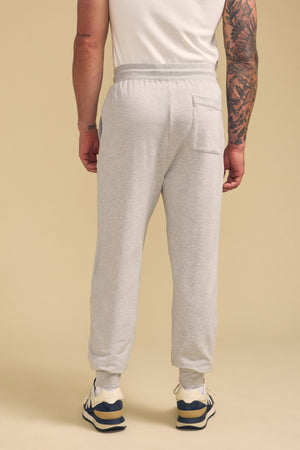 A person wearing the JACOBY JOGGER by Velvet by Graham & Spencer in light gray, paired with a white T-shirt and sneakers, stands with their back to the camera against a beige background.