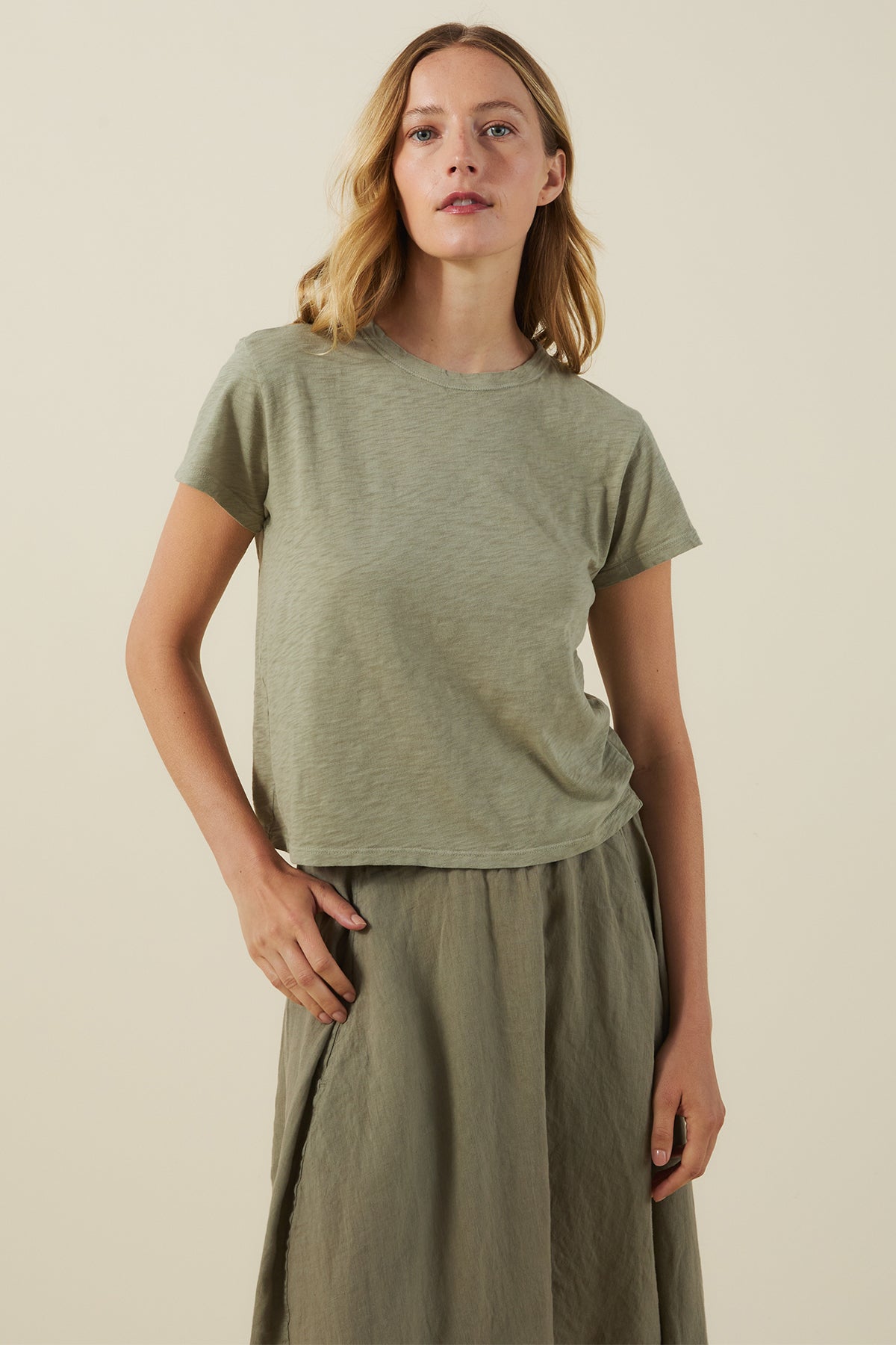 A woman stands against a plain background wearing the MARIKA TEE in light green by Velvet by Graham & Spencer, crafted from cotton slub with a relaxed boxy fit, perfectly paired with a matching green skirt.