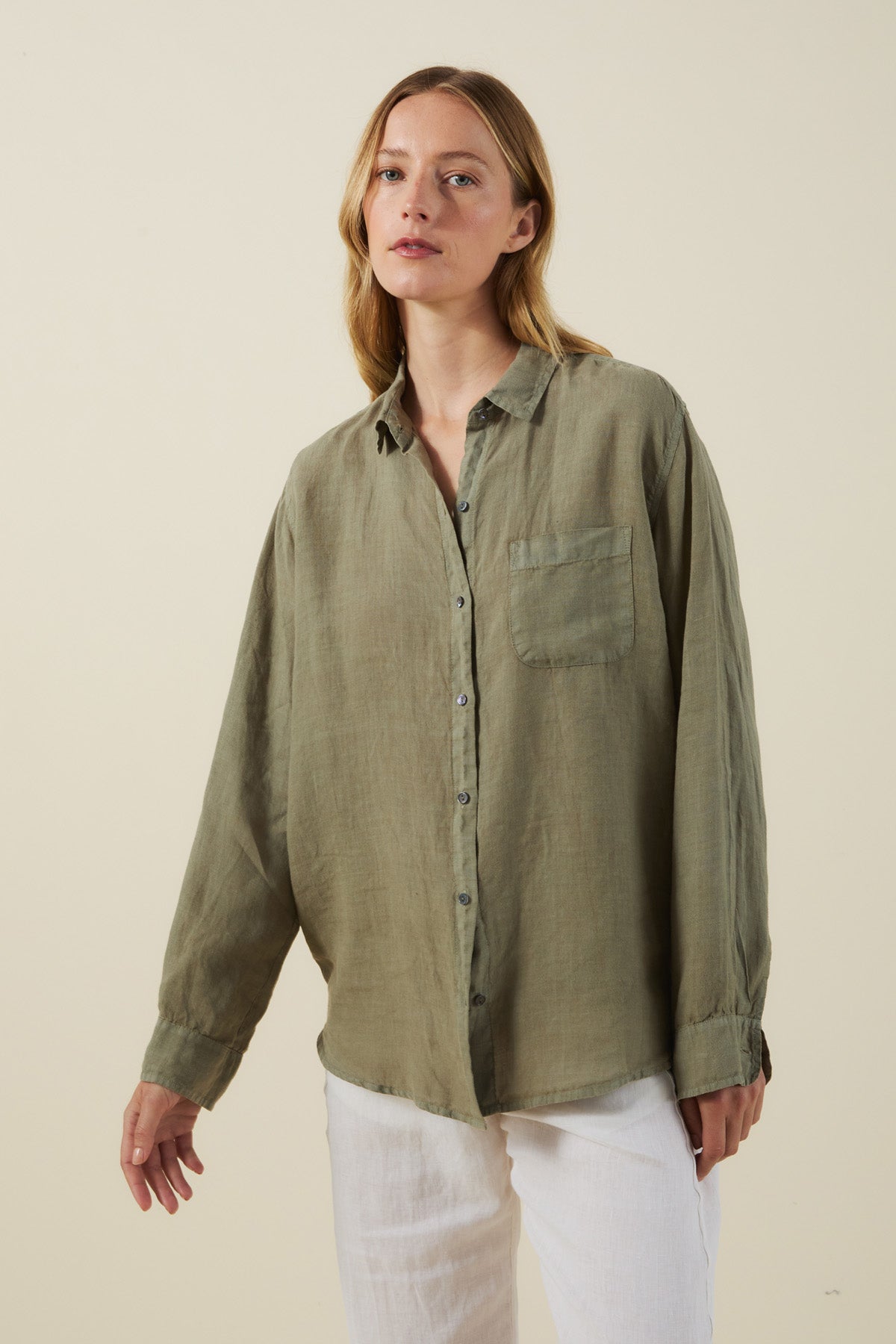 A woman wears the MULHOLLAND LINEN SHIRT by Velvet by Jenny Graham—an olive green, breathable linen button-up with a chest pocket—paired with white pants against a plain light background.-41645087391937