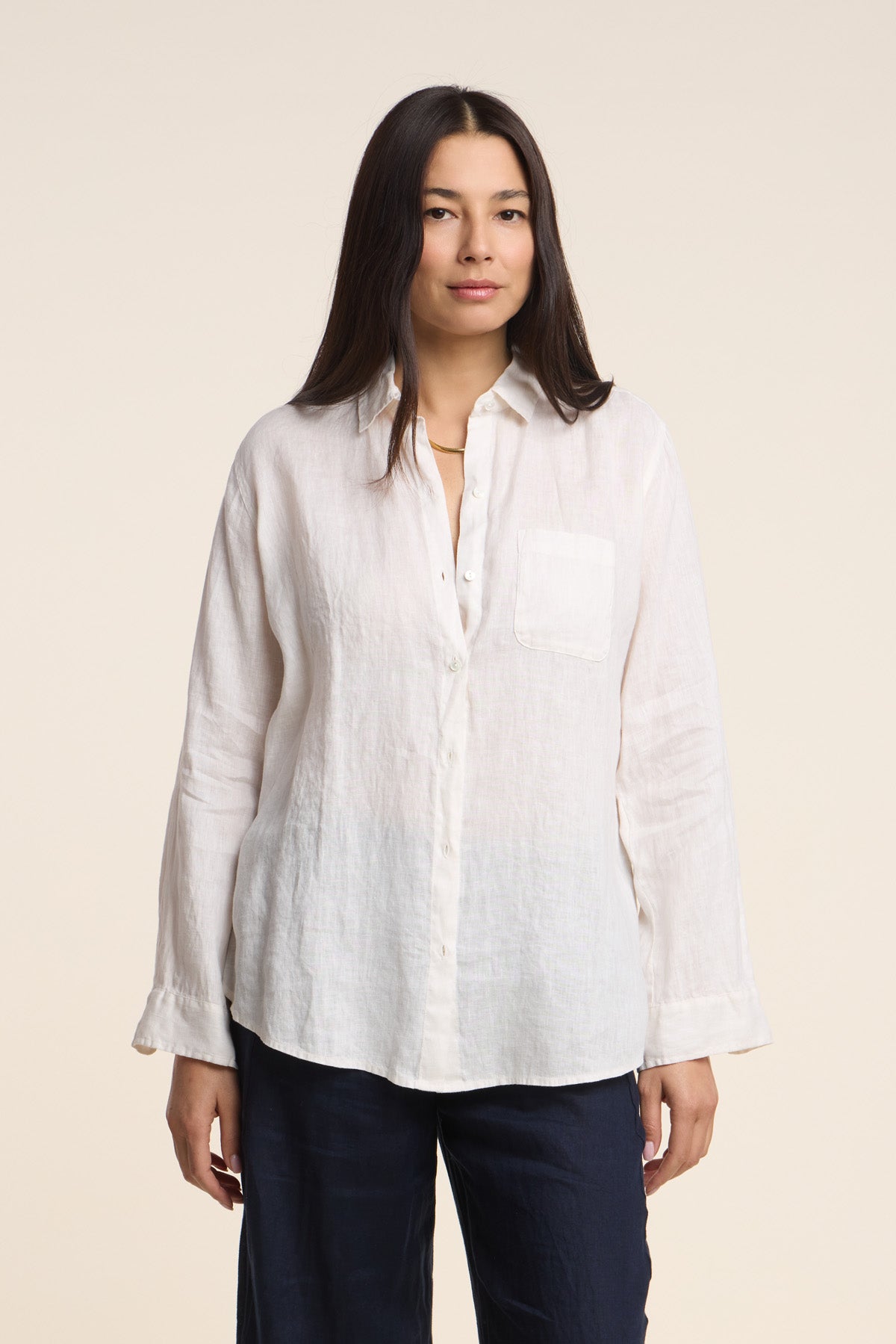 A woman faces forward against a plain light background, wearing the MULHOLLAND LINEN SHIRT by Velvet by Jenny Graham, a white woven linen button-up, paired with dark pants.