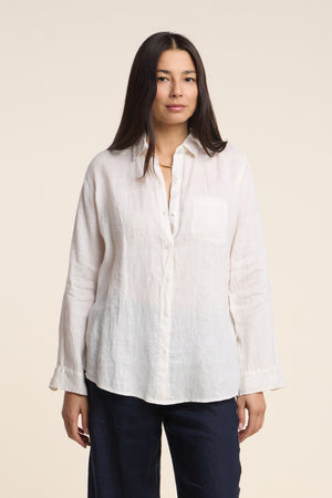 A woman faces forward against a plain light background, wearing the MULHOLLAND LINEN SHIRT by Velvet by Jenny Graham, a white woven linen button-up, paired with dark pants.