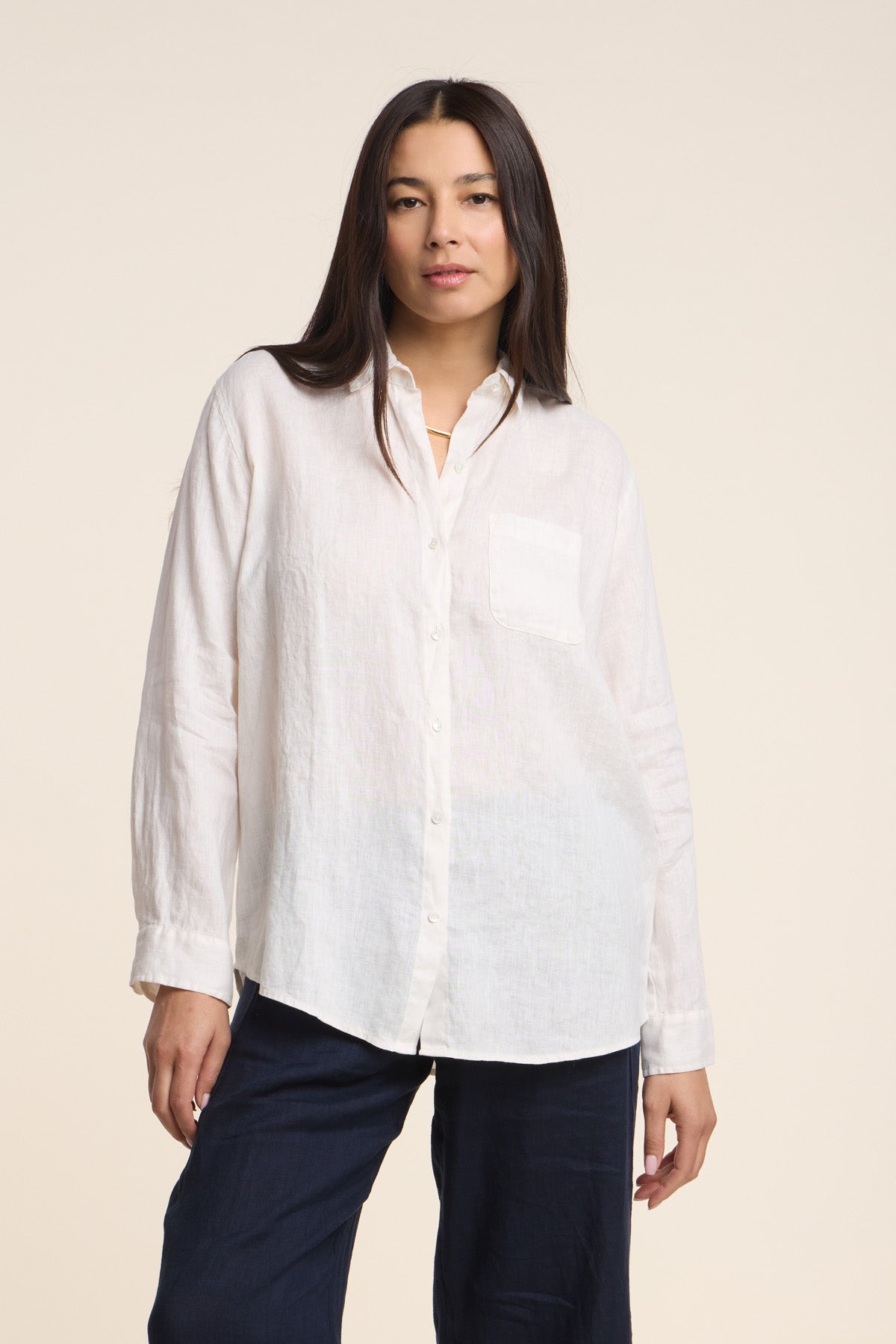 A woman wearing the MULHOLLAND LINEN SHIRT by Velvet by Jenny Graham— a long-sleeve woven linen button-up with a pocket—paired with dark pants, stands against a plain light background.