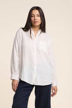 A woman wearing the MULHOLLAND LINEN SHIRT by Velvet by Jenny Graham— a long-sleeve woven linen button-up with a pocket—paired with dark pants, stands against a plain light background.