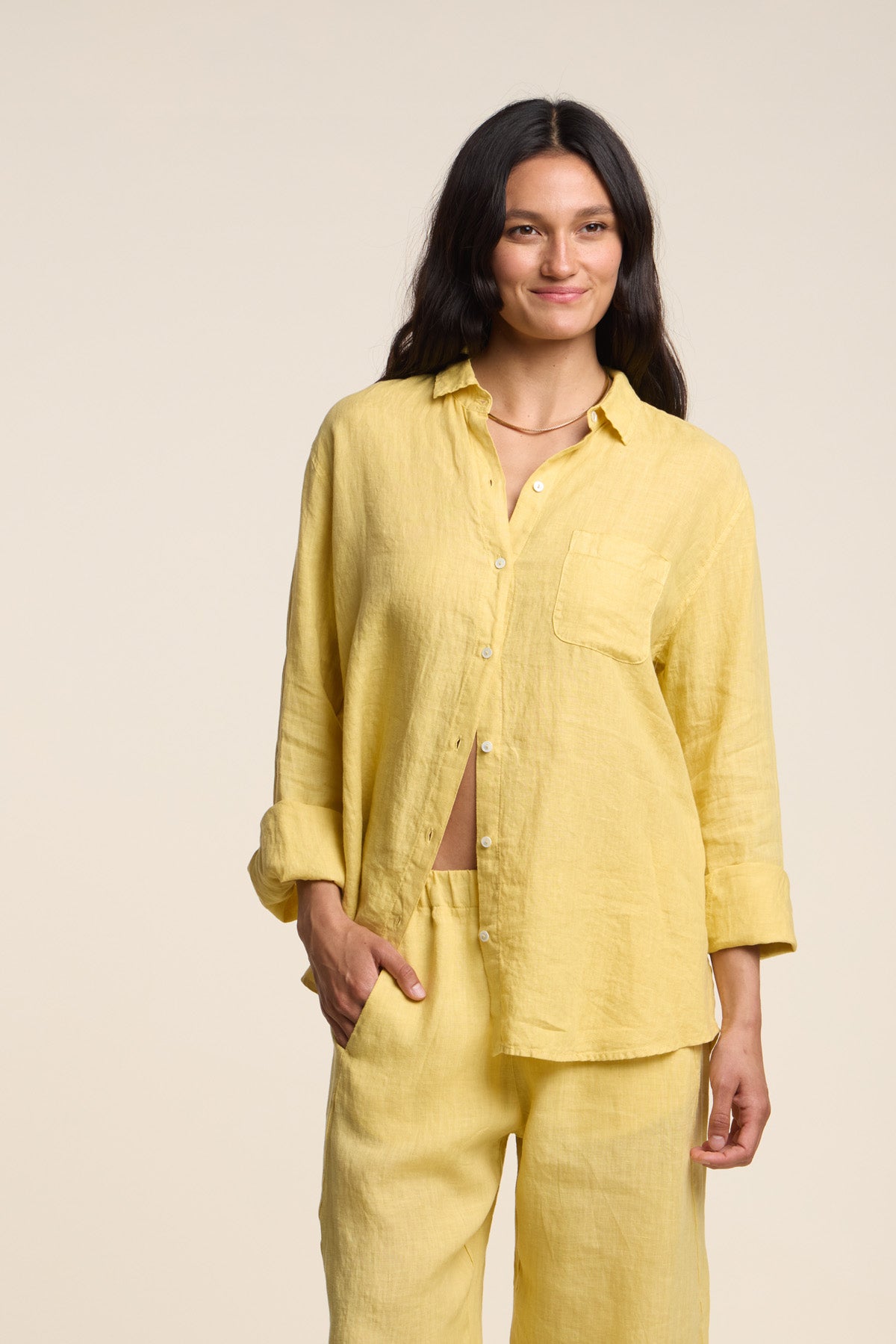 A woman stands against a plain background wearing the MULHOLLAND LINEN SHIRT by Velvet by Jenny Graham, styled loosely with matching pants and her left hand in her pocket.-41527102603457