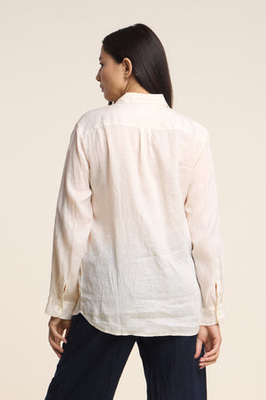 A woman faces away from the camera, wearing the MULHOLLAND LINEN SHIRT by Velvet by Jenny Graham with dark pants, set against a plain backdrop.