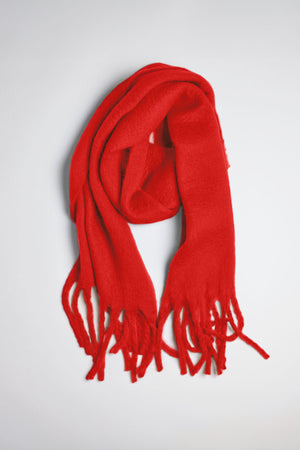 The CHIC SOLID SCARF by Velvet by Graham & Spencer, a vibrant red accessory with fringed ends, is laid flat on a light gray surface.