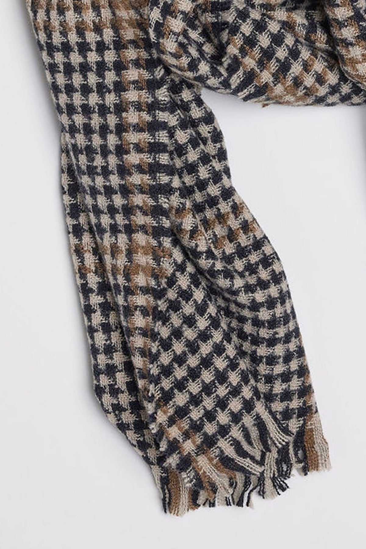   A close-up of the PEAK SCARF by Velvet by Graham & Spencer, featuring a black, white, and brown houndstooth pattern with frayed edges. 