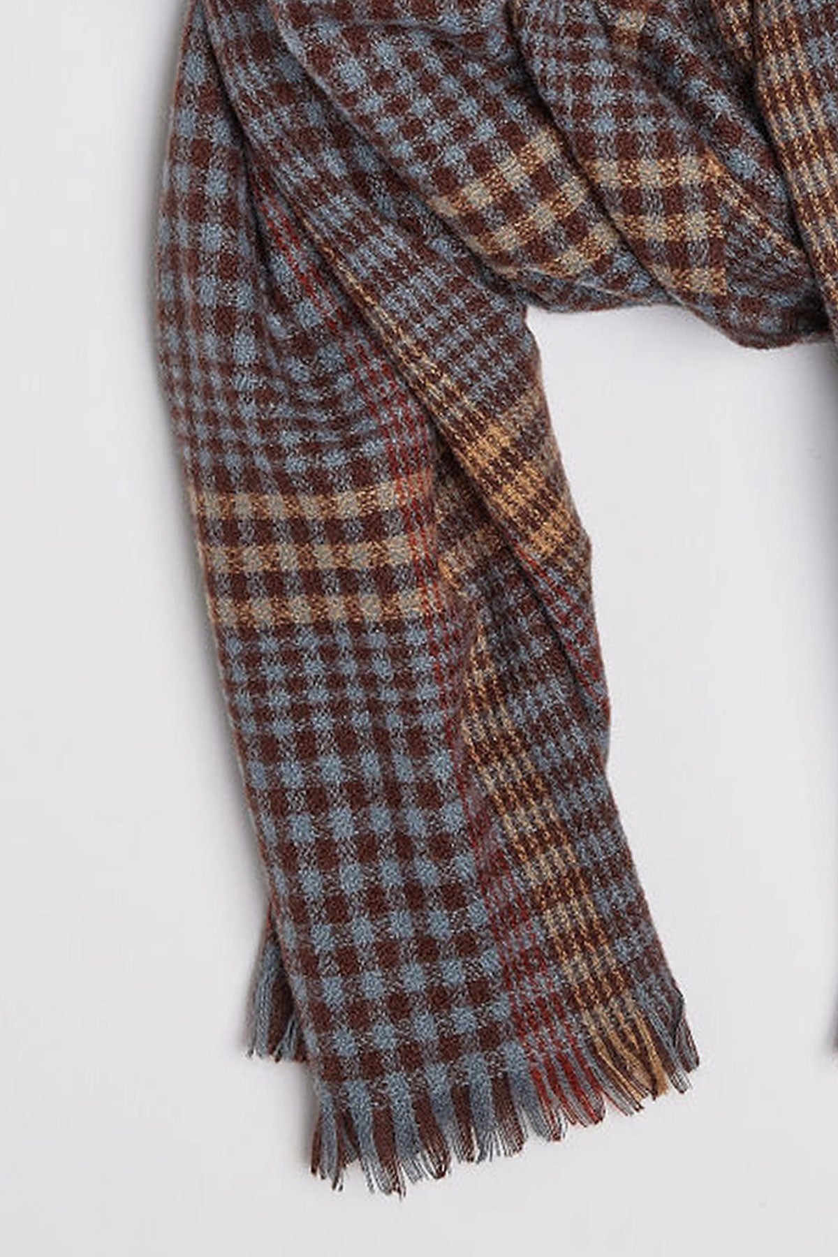   A close-up of the STOWE SCARF by Velvet by Graham & Spencer, showcasing its checkered pattern in shades of brown, blue, and beige. The woolen scarf features frayed edges. 