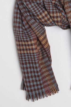 A close-up of the STOWE SCARF by Velvet by Graham & Spencer, showcasing its checkered pattern in shades of brown, blue, and beige. The woolen scarf features frayed edges.