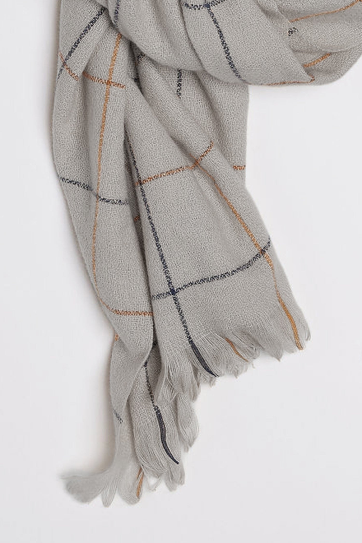   A close-up of the HUDSON WINDOWPANE SCARF by Velvet by Graham & Spencer, showcasing its light gray color with a plaid pattern of thin black and brown lines, and fringed ends. 