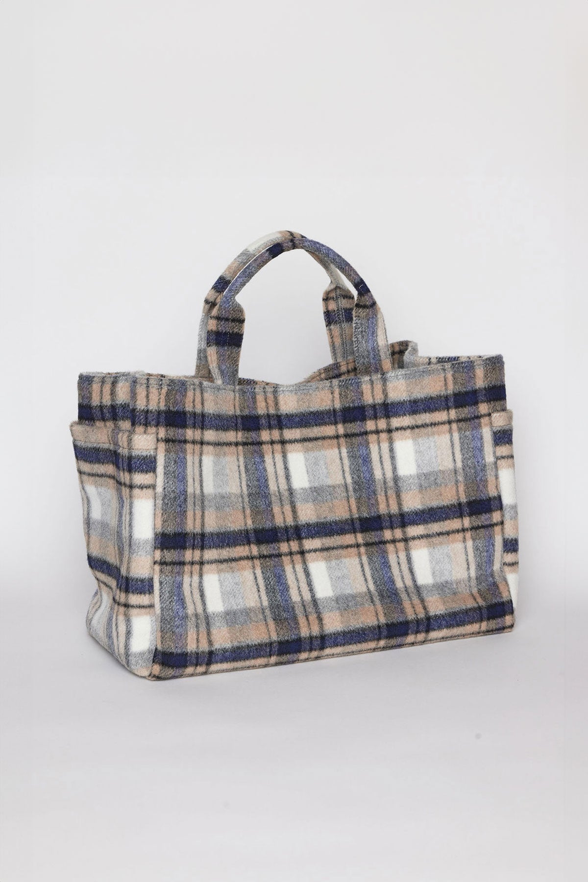   The PLAID TOTE by Velvet by Graham & Spencer is a fabric tote bag with handles, featuring a design of light and dark brown, blue, and white checks. 